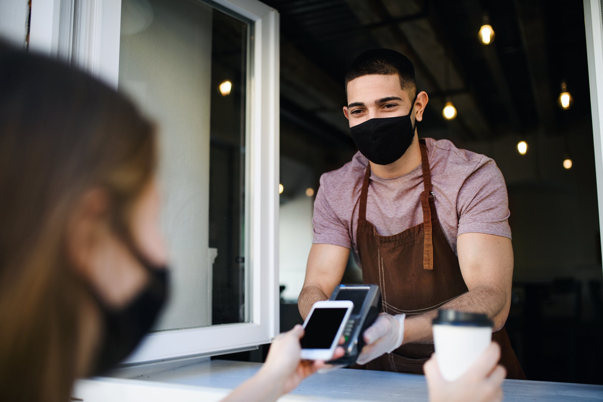 Unrecognizable customer paying for coffee with smartphone.